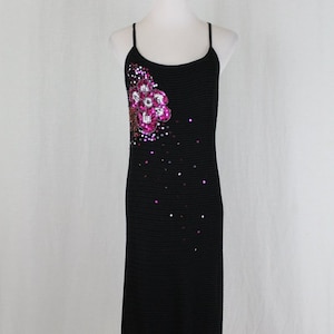 May include: A black knit midi dress with a floral sequin embellishment on the bodice. The dress has thin spaghetti straps and a loose fit.
