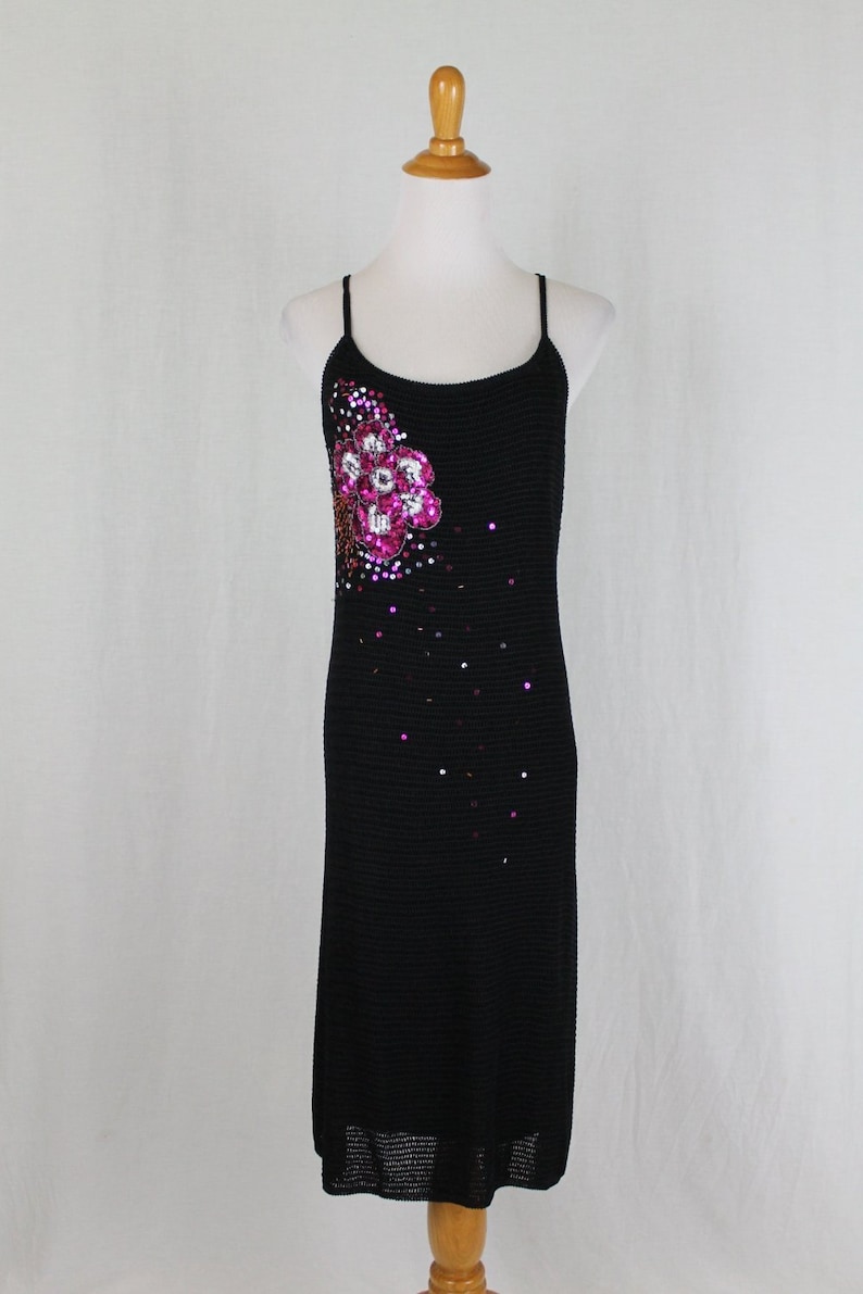 May include: A black knit midi dress with a floral sequin embellishment on the bodice. The dress has thin spaghetti straps and a loose fit.