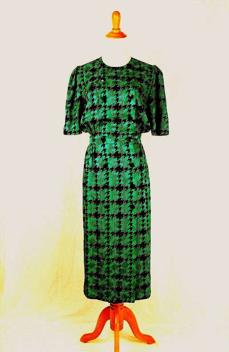 May include: A green and black houndstooth dress with short sleeves. The dress is on a wooden dress form.