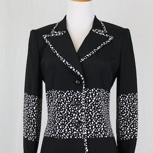 May include: A black and white polka dot blazer with a contrasting black collar and cuffs. The blazer has a button-up front and a fitted silhouette.