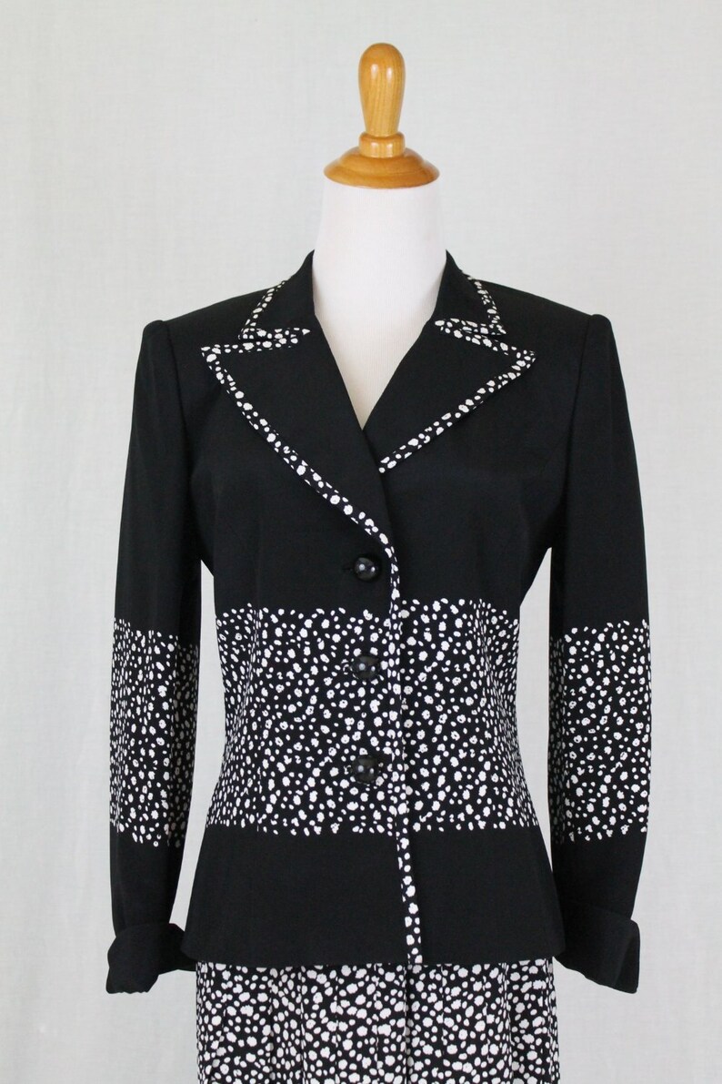 May include: A black and white polka dot blazer with a contrasting black collar and cuffs. The blazer has a button-up front and a fitted silhouette.