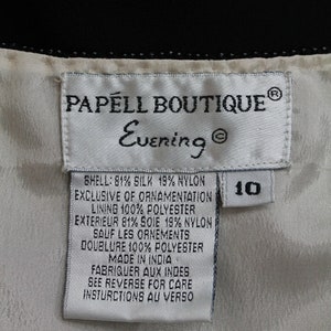 Pode incluir: Etiqueta branca com texto preto que diz "PAPELL BOUTIQUE&reg; Evening&reg;" e lista o conte&uacute;do do tecido: "SHELL: 81 % SEDA 19 % NYLON EXCLUSIVE OF ORNAMENTATION LINING 100 % POLI&Eacute;STER EXTERIEUR 81 % SOIE 19 % NYLON SAUF LES ORNEMENTS DOUBLURE 100 % POLI&Eacute;STER MADE IN INDIA FABRIQUER AUX INDES SEE REVERSE FOR CARE INSTRUCTIONS AU VERSO". A etiqueta tamb&eacute;m tem uma etiqueta branca com texto preto que diz "10".