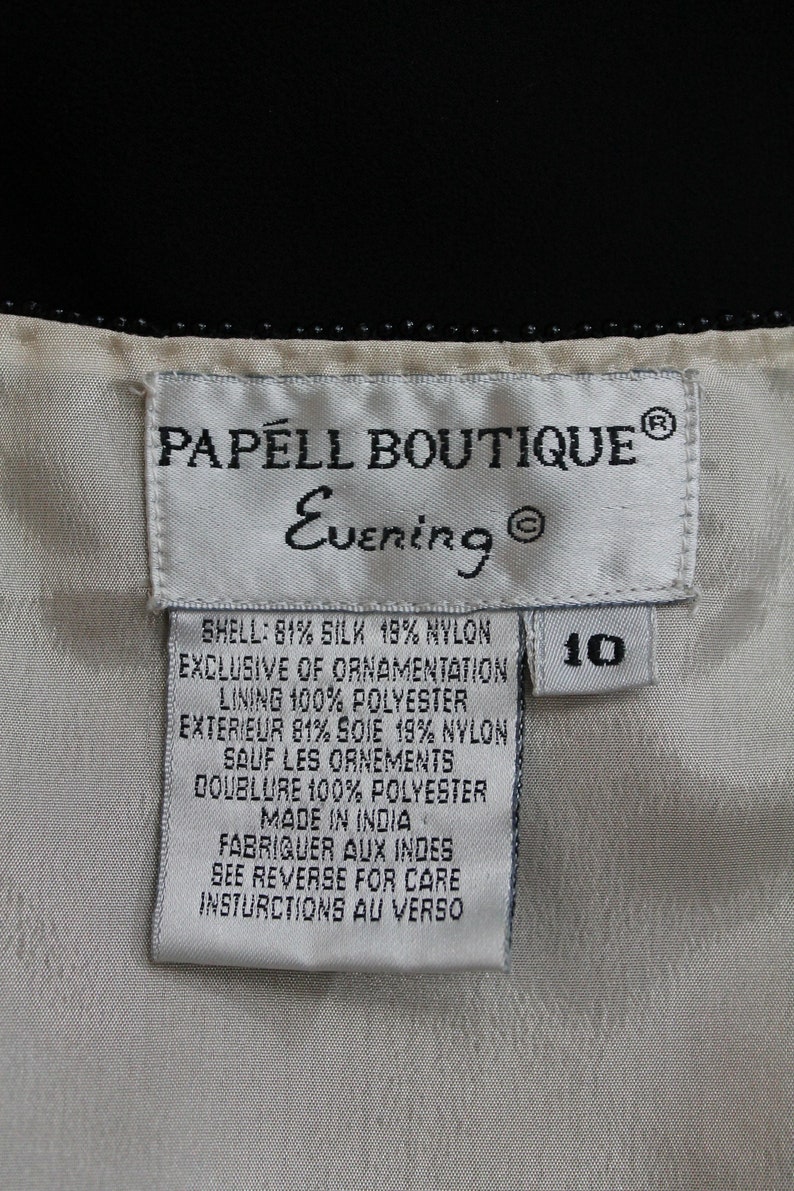 Pode incluir: Etiqueta branca com texto preto que diz "PAPELL BOUTIQUE&reg; Evening&reg;" e lista o conte&uacute;do do tecido: "SHELL: 81 % SEDA 19 % NYLON EXCLUSIVE OF ORNAMENTATION LINING 100 % POLI&Eacute;STER EXTERIEUR 81 % SOIE 19 % NYLON SAUF LES ORNEMENTS DOUBLURE 100 % POLI&Eacute;STER MADE IN INDIA FABRIQUER AUX INDES SEE REVERSE FOR CARE INSTRUCTIONS AU VERSO". A etiqueta tamb&eacute;m tem uma etiqueta branca com texto preto que diz "10".