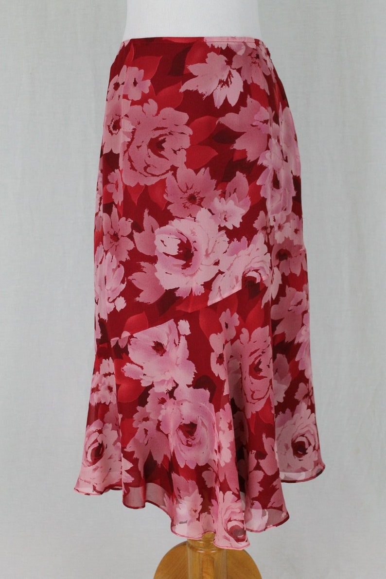 May include: A red and pink floral skirt with a flowing hemline. The skirt is made of a lightweight fabric and has a casual, feminine style.