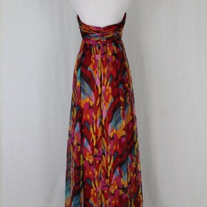 May include: A long, flowing halter dress with a vibrant abstract print in shades of red, orange, yellow, blue, and pink. The dress is made of a lightweight, sheer fabric and has a flowing silhouette.