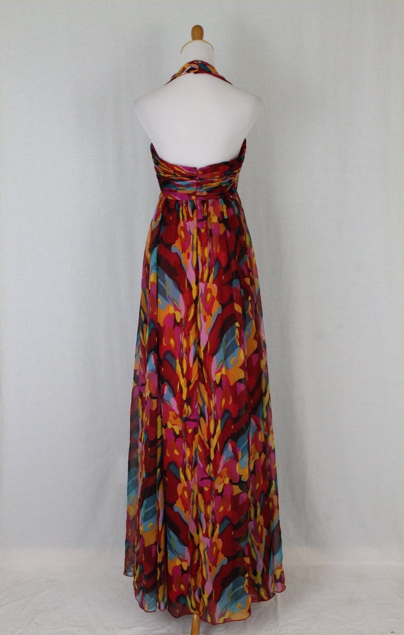 May include: A long, flowing halter dress with a vibrant abstract print in shades of red, orange, yellow, blue, and pink. The dress is made of a lightweight, sheer fabric and has a flowing silhouette.