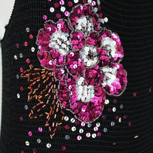 May include: A black knit top with a large pink and white sequin flower design. The flower is embellished with small brown beads.