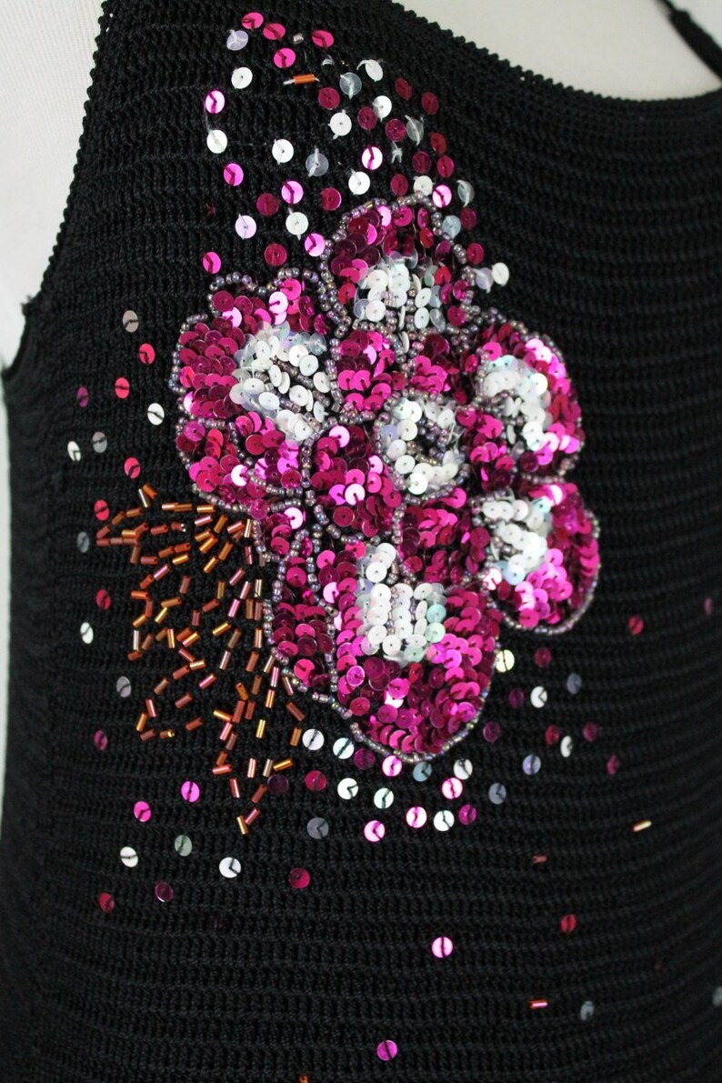 May include: A black knit top with a large pink and white sequin flower design. The flower is embellished with small brown beads.