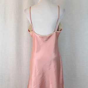 May include: A pink satin slip dress with a lace trim around the neckline. The dress is sleeveless and has a fitted bodice and a flowing skirt.