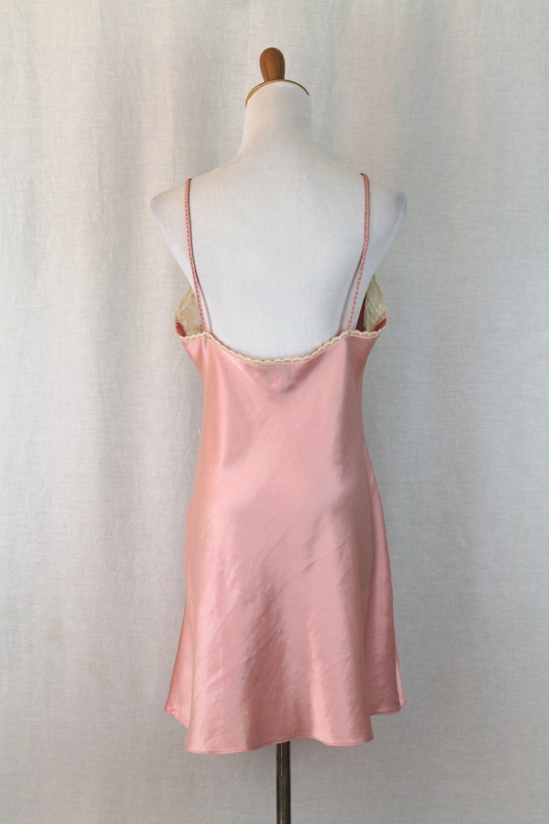 May include: A pink satin slip dress with a lace trim around the neckline. The dress is sleeveless and has a fitted bodice and a flowing skirt.