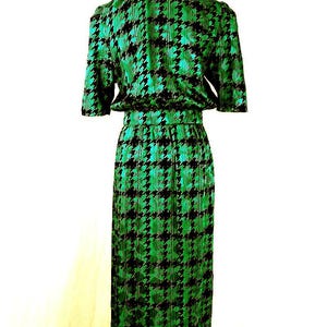 May include: A green and black houndstooth print dress with short sleeves and a fitted silhouette. The dress is on a mannequin and has a cinched waist.