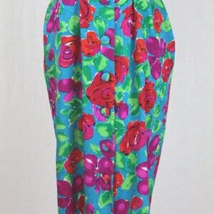 Puede incluir: Un vestido azul turquesa con estampado floral con flores rojas, rosas y verdes. El vestido tiene un frente abotonado y un cintur&oacute;n.
