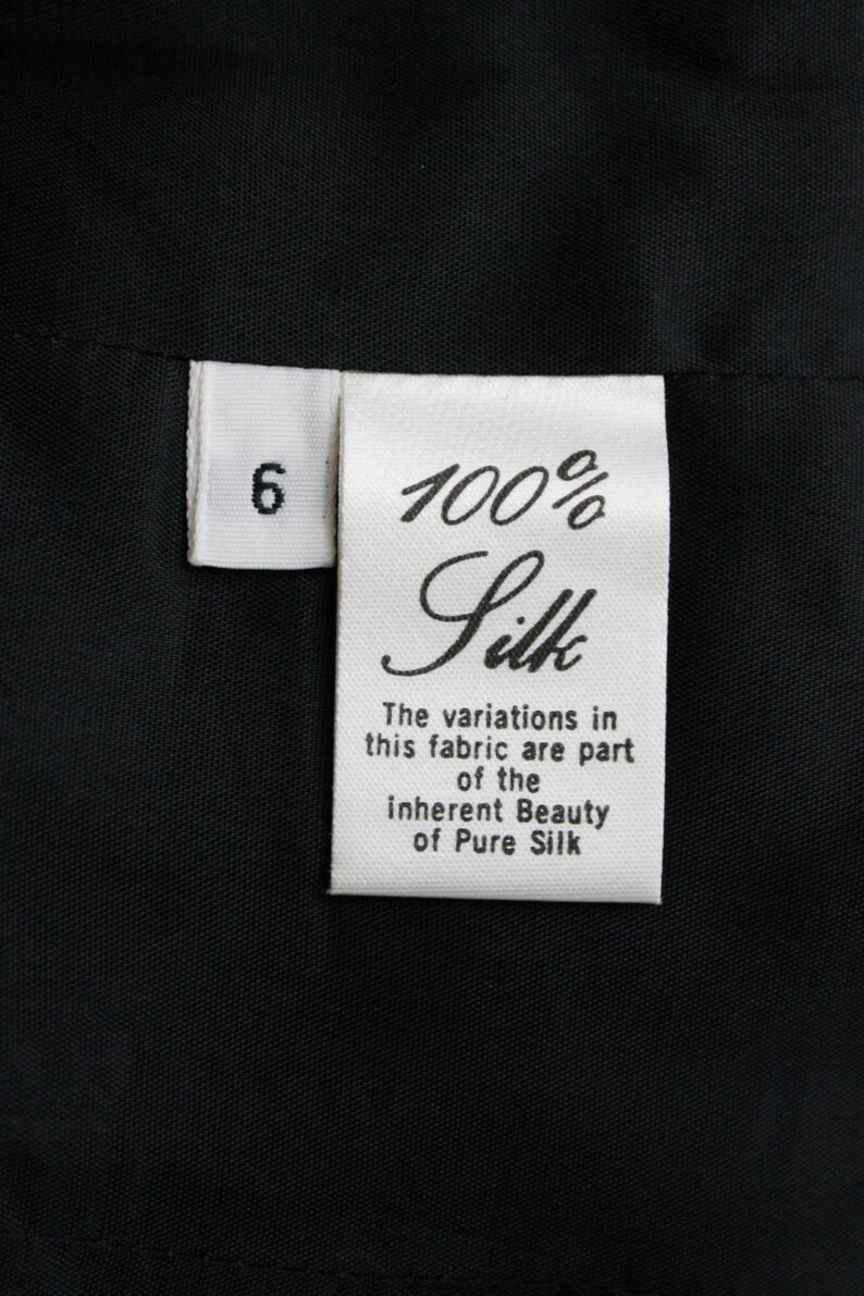 May include: White fabric tag with black text that reads "6 100% Silk The variations in this fabric are part of the inherent Beauty of Pure Silk"