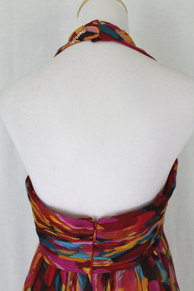 May include: Back view of a halter-style dress with a colourful abstract print. The dress has a zip closure at the back and a beaded neckline.