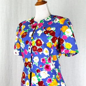 May include: A blue floral print skirt suit with short sleeves and a button-up front. The suit features a vibrant floral pattern in shades of red, yellow, pink, white, and green.