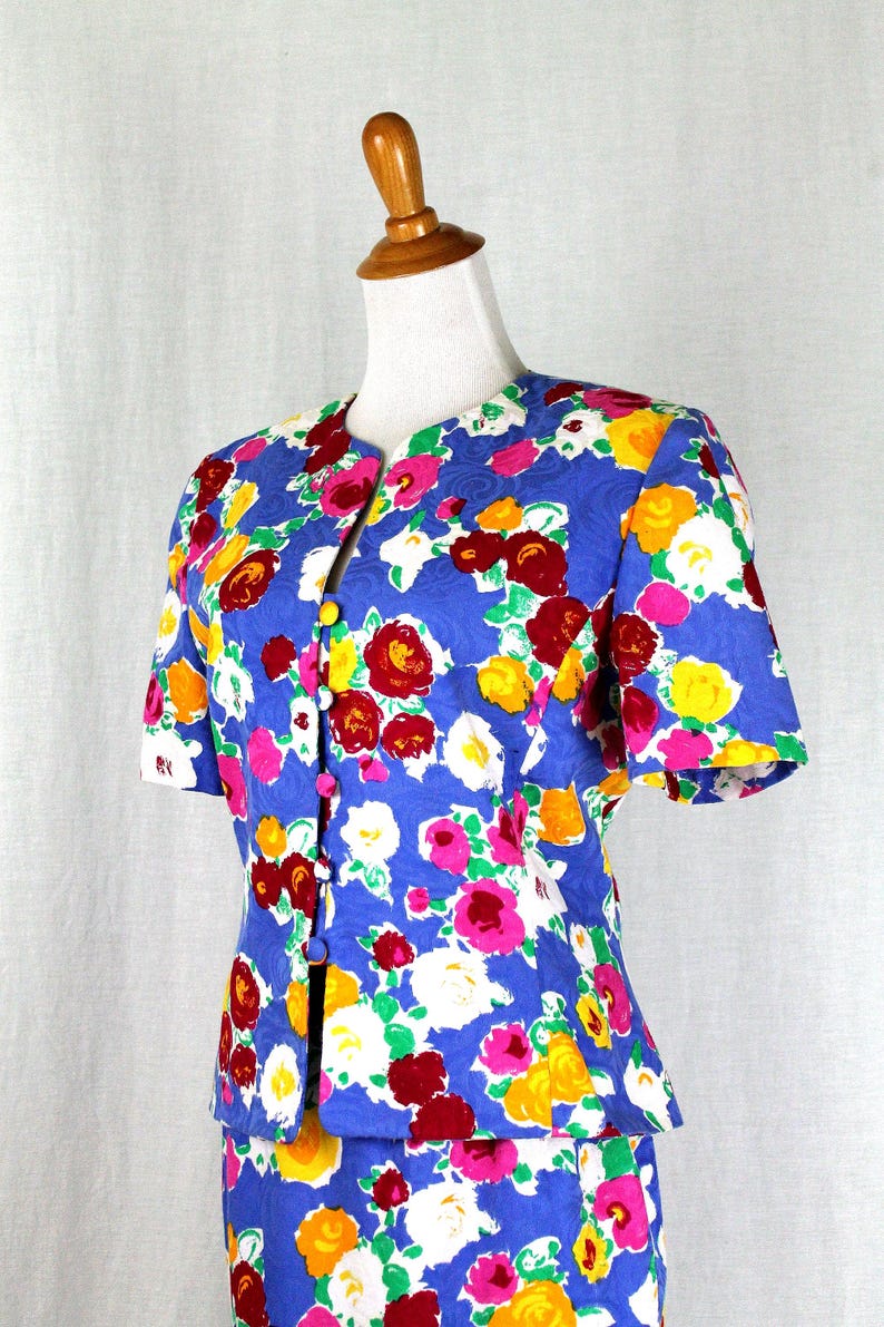May include: A blue floral print skirt suit with short sleeves and a button-up front. The suit features a vibrant floral pattern in shades of red, yellow, pink, white, and green.