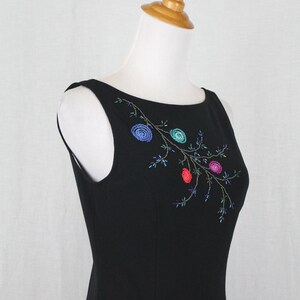 K&ouml;nnte beinhalten: Ein schwarzes, &auml;rmelloses Kleid mit einem floralen Stickmuster, das mit bunten Perlen verziert ist. Die Stickerei befindet sich auf der Vorderseite des Kleides und zeigt einen Zweig mit Bl&auml;ttern und Bl&uuml;ten.