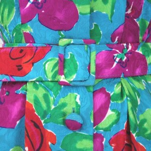 Puede incluir: Un vestido azul con estampado floral en tonos rosa, rojo y verde. El vestido tiene un cintur&oacute;n con una hebilla plateada.
