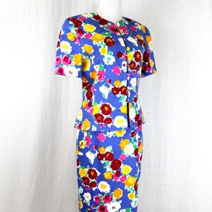 May include: A blue floral print skirt suit with a short-sleeved jacket and a knee-length skirt. The suit features a colorful floral pattern with red, yellow, white, and pink flowers on a blue background.