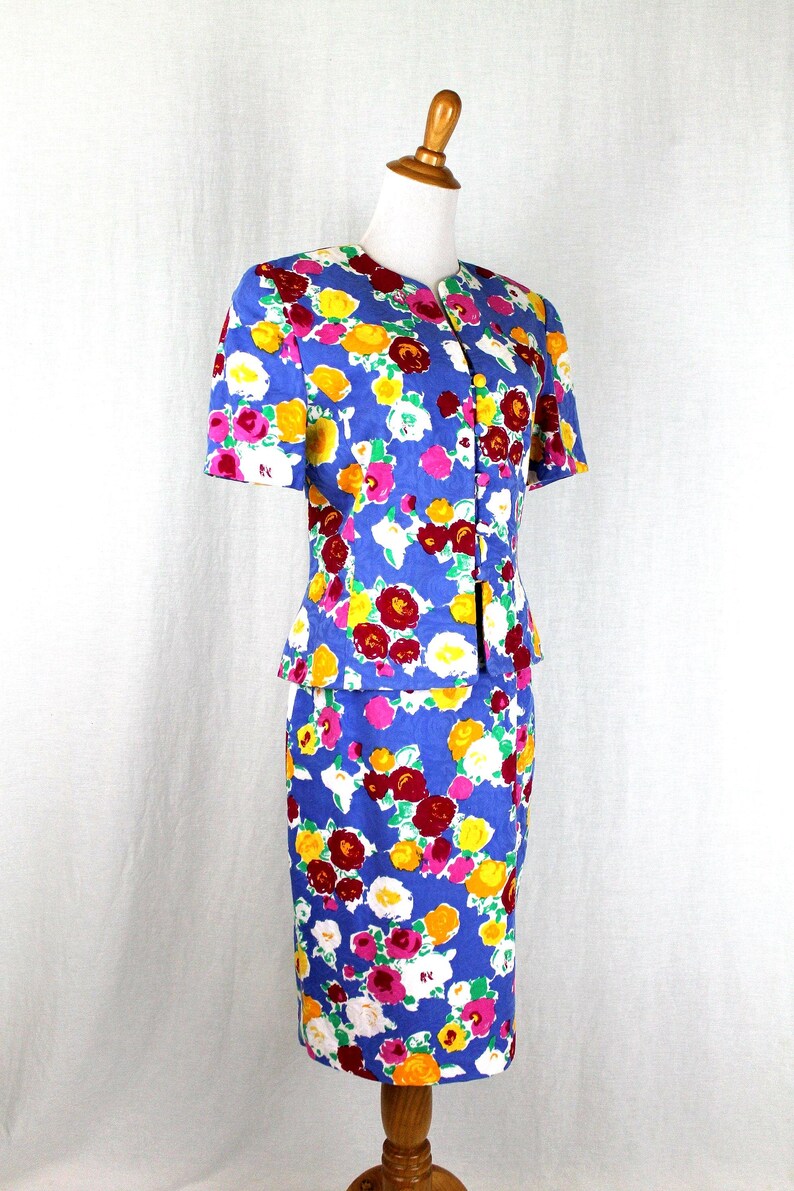 May include: A blue floral print skirt suit with a short-sleeved jacket and a knee-length skirt. The suit features a colorful floral pattern with red, yellow, white, and pink flowers on a blue background.