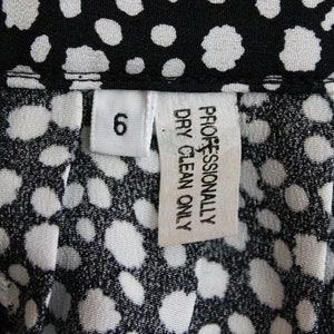 May include: White tag with black text that reads "Professionally Dry Clean Only" and a white tag with black text that reads "6". The tags are on a black and white fabric with a polka dot pattern.