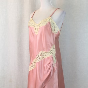 May include: A pink satin slip dress with delicate white lace trim. The dress has a V-neckline and adjustable straps.