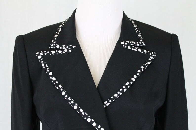 May include: A black blazer with a white polka dot trim around the collar.