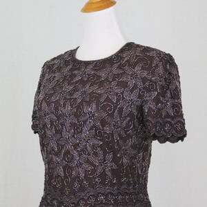 May include: A brown beaded top with a floral pattern and scalloped edges. The top has short sleeves and a round neckline.