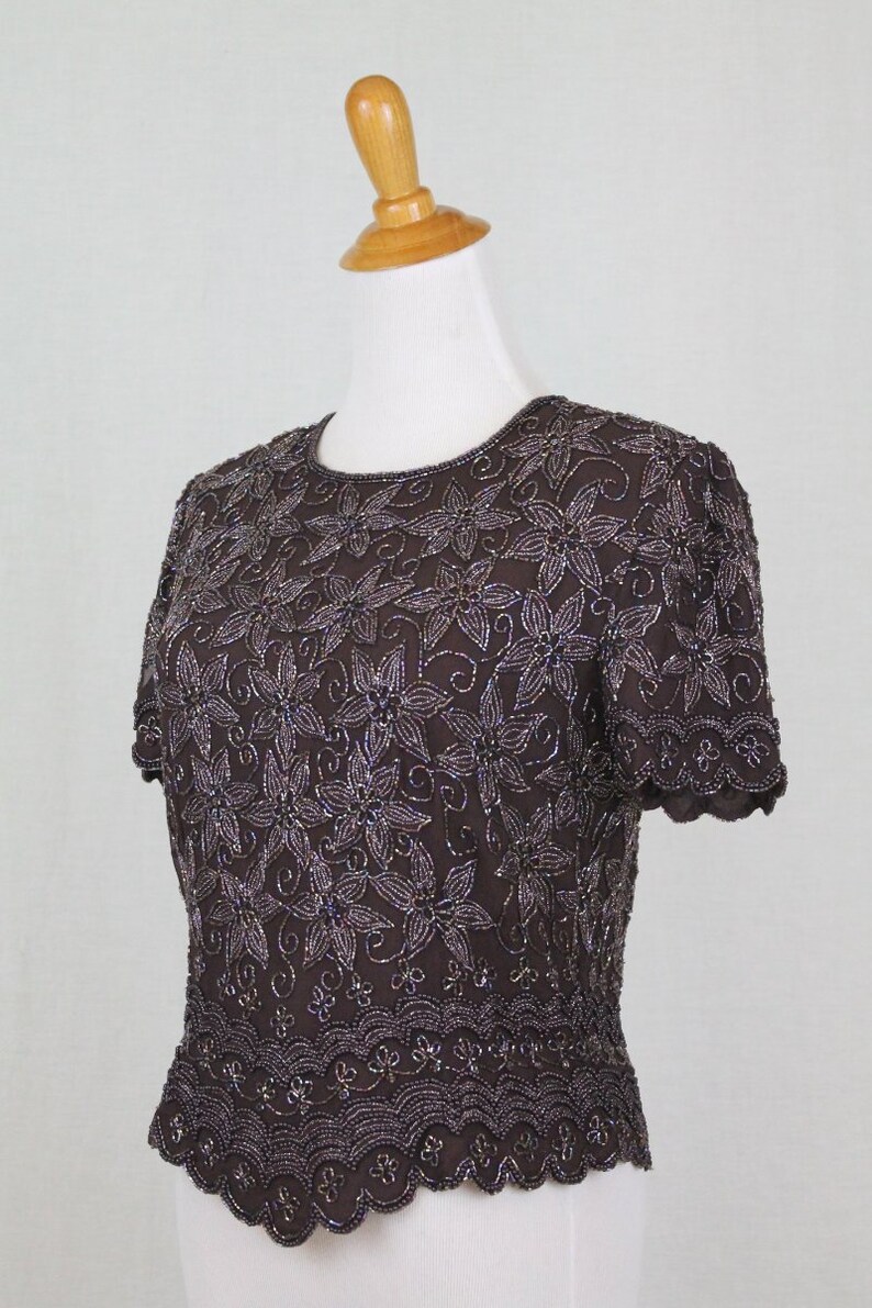 May include: A brown beaded top with a floral pattern and scalloped edges. The top has short sleeves and a round neckline.