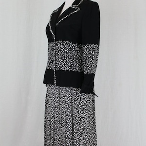 May include: A black and white polka dot skirt suit with a pleated skirt. The jacket has a black collar and a black band across the middle.