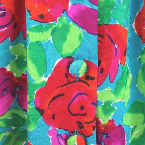Puede incluir: Primer plano de una tela azul turquesa con un patr&oacute;n floral en tonos rojos, rosas, verdes y blancos. Tres botones azul turquesa est&aacute;n cosidos en la parte delantera de la tela.