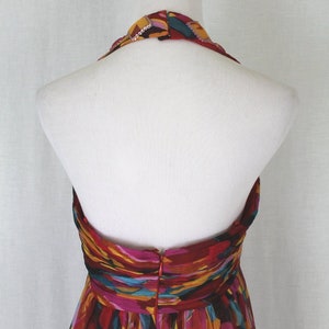 May include: A halter-style dress with a colourful abstract print in shades of red, orange, yellow, pink, and blue. The dress has a fitted bodice and a flowing skirt.