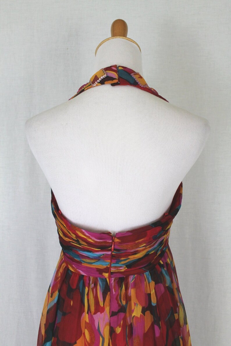 May include: A halter-style dress with a colourful abstract print in shades of red, orange, yellow, pink, and blue. The dress has a fitted bodice and a flowing skirt.