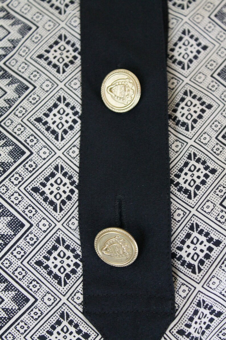 May include: A black fabric with a white and black geometric pattern. Two gold buttons with a crest design are attached to the fabric.