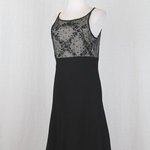 Pode incluir: Um vestido preto sem mangas com um corpete de renda transparente com um padr&atilde;o floral. A saia &eacute; em A e chega ao joelho.