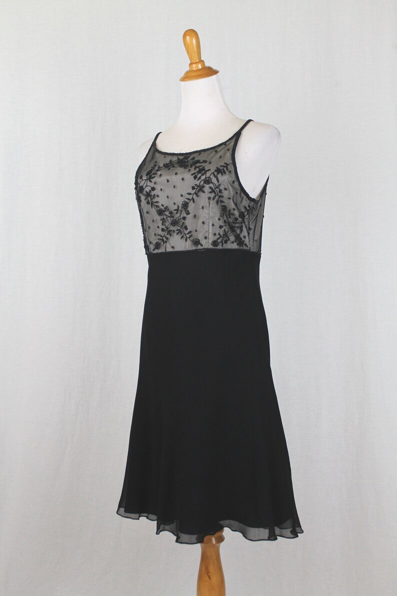 Pode incluir: Um vestido preto sem mangas com um corpete de renda transparente com um padr&atilde;o floral. A saia &eacute; em A e chega ao joelho.