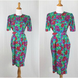 Puede incluir: Un vestido azul turquesa con estampado floral con grandes rosas rojas y rosas. El vestido tiene manga corta, cierre frontal con botones y un cintur&oacute;n a juego.