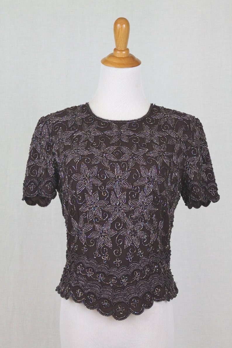 May include: A brown beaded top with a floral design. The top has short sleeves and a scalloped hem.