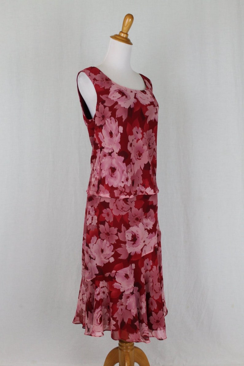 May include: A sleeveless red and pink floral print dress with a ruffled hemline. The dress is on a white background.