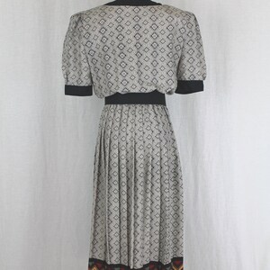 May include: A black and white patterned dress with a black waistband and a colorful geometric print at the hem. The dress has a fitted bodice and a pleated skirt.