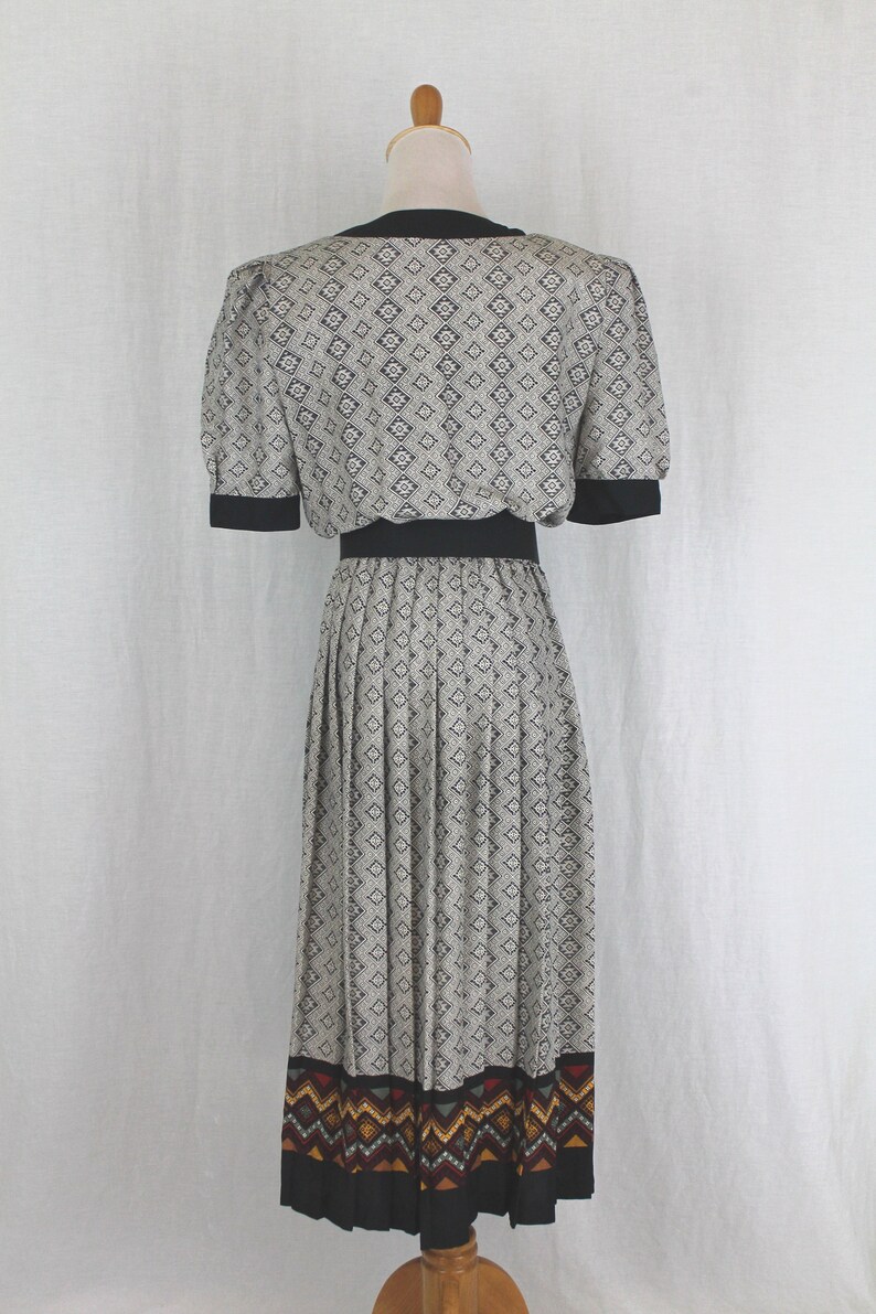 May include: A black and white patterned dress with a black waistband and a colorful geometric print at the hem. The dress has a fitted bodice and a pleated skirt.