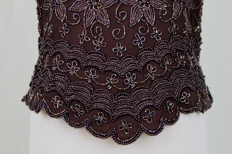 May include: A brown beaded top with a scalloped hem and a floral design. The beads are iridescent and create a shimmering effect.