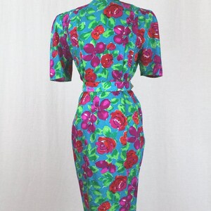 Puede incluir: Un vestido azul turquesa con estampado floral con rosas rosas y rojas. El vestido tiene manga corta y una silueta ajustada.