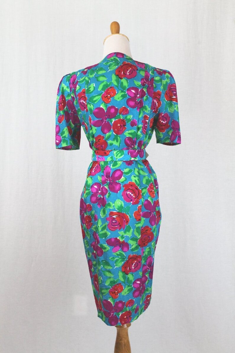 Puede incluir: Un vestido azul turquesa con estampado floral con rosas rosas y rojas. El vestido tiene manga corta y una silueta ajustada.