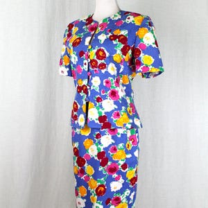 May include: A blue floral print skirt suit with short sleeves and a button-up front. The skirt is knee-length and the jacket is fitted.