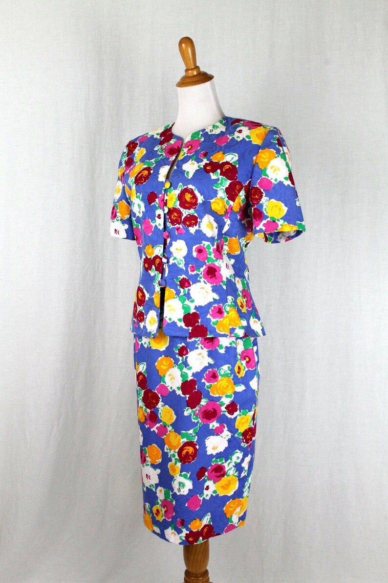 May include: A blue floral print skirt suit with short sleeves and a button-up front. The skirt is knee-length and the jacket is fitted.