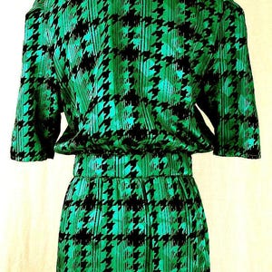 May include: A green and black dress with a houndstooth pattern. The dress has a short sleeve and a fitted waist.