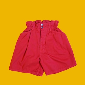 Op de afbeelding: Felrode shorts met hoge taille, een gerimpelde tailleband en een sluiting met twee knopen. De shorts hebben twee voorzakken en een klassieke, casual stijl. De shorts zijn gemaakt van een stevige stof en staan tegen een gele achtergrond.