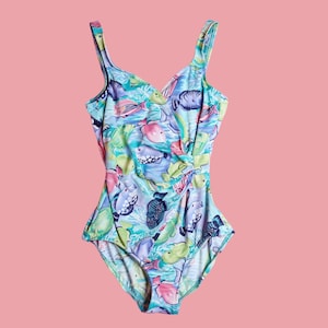 May include: A one-piece swimsuit with a colorful fish pattern in shades of blue, green, pink, and purple. The swimsuit has a V-neckline and thin shoulder straps. The fabric is a soft, lightweight material.