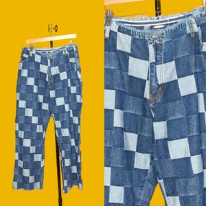 May include: A pair of blue denim jeans with a checkered pattern. The jeans are made of different shades of blue denim and are sewn together to create a checkered pattern.